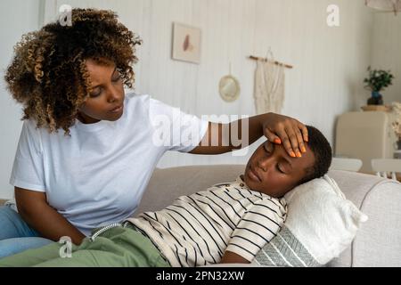 Affectueuse femme afro-américaine inquiète mère prenant soin de l'enfant malade fils à la maison Banque D'Images