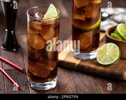 Cocktail au rhum et au cola dans de grands verres avec une tranche de citron vert sur une table rustique en bois Banque D'Images