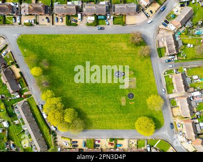 Vue aérienne vers le haut d'un espace vert central et d'un petit terrain de jeu. Entouré de maisons semi-individuelles dans un village typiquement anglais. Banque D'Images