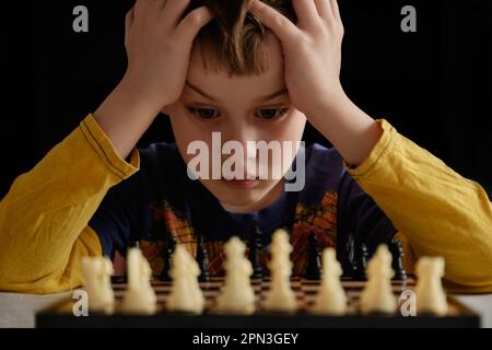 Mignon petit garçon joue aux échecs. Concept d'éducation, jeu intellectuel. Garçon concentré développant la stratégie d'échecs. Tournoi d'échecs, leçon, entraînement. Banque D'Images