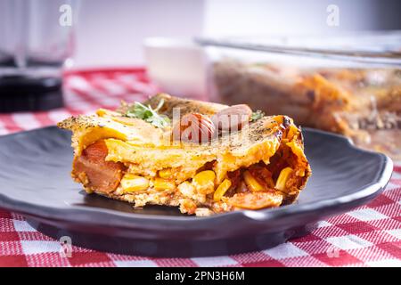 Coupez un morceau de tarte aux saucisses dans un blender, plat typiquement brésilien. Ingrédients : lait, blé, huile, saucisse et maïs. Sur une nappe à carreaux. Vue avant. Banque D'Images