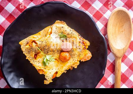 Coupez un morceau de tarte aux saucisses dans un blender, plat typiquement brésilien. Ingrédients : lait, blé, huile, saucisse et maïs. Sur une nappe à carreaux. Vue de dessus. Banque D'Images