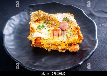 Coupez un morceau de tarte aux saucisses dans un blender, plat typiquement brésilien. Ingrédients : lait, blé, huile, saucisse et maïs. Sur une nappe à carreaux. Perspective v Banque D'Images