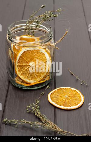 Frites d'orange dans un pot en verre. Sécher des branches de thym sur la table. Arrière-plan en bois sombre. Banque D'Images