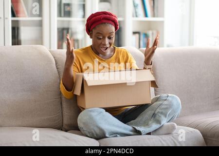 Femme afro-américaine excitée regardant à l'intérieur de la boîte en papier colis Banque D'Images