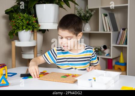 Un enfant d'âge préscolaire joue avec une mosaïque, construit des figures sur une planche, martelant des ongles avec un marteau sur des parties multicolores du concepteur Banque D'Images