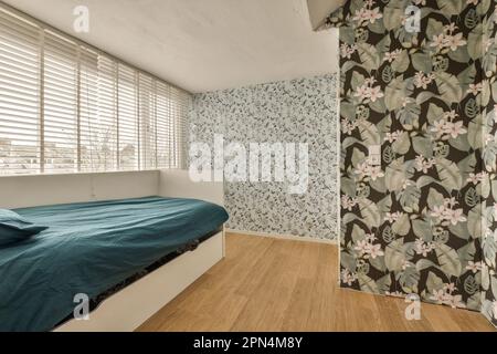 une chambre avec papier peint floral sur les murs et parquet devant le lit, stores derrière Banque D'Images