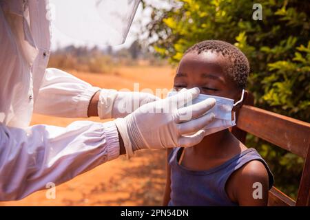 Un médecin met un masque chirurgical sur un enfant lors d'une visite pédiatrique en Afrique. Banque D'Images