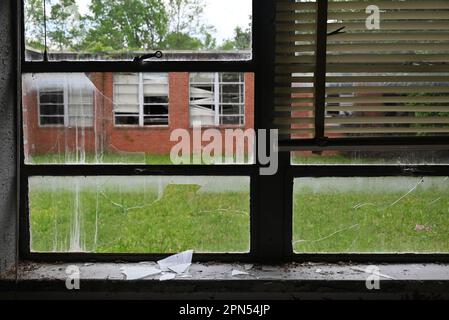 Vue sur une fenêtre de salle de classe cassée dans la cour d'une école qui a été abandonnée depuis 2001. Banque D'Images