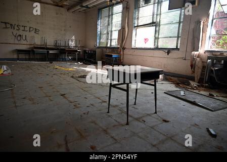 Un bureau d'étudiant est installé dans une salle de classe remplie de débris dans une école vandalisée et abandonnée depuis 2001. Banque D'Images