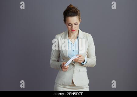 femme d'affaires moderne pensive dans un costume d'affaires léger avec euros packs d'argent sur fond gris. Banque D'Images