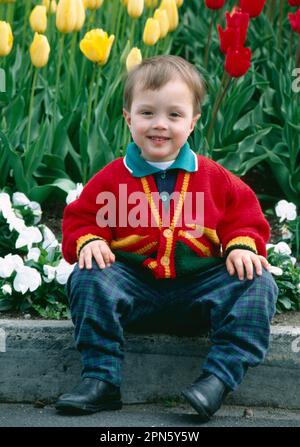 Adorable garçon de 3 ans dans un chandail coloré sur fond de tulipes dans un jardin botanique Banque D'Images