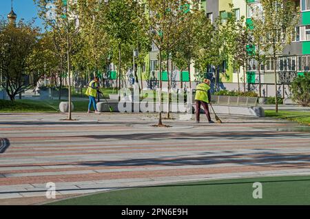 Des concierges balayant la zone de loisirs d'un complexe résidentiel de plusieurs étages lors d'une journée d'automne ensoleillée. Dnipro, Ukraine - 15 septembre 2021 Banque D'Images