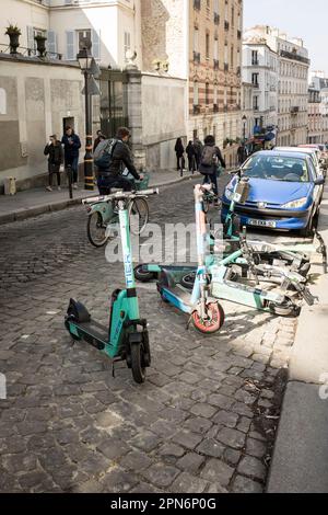 Location de trottinettes de différentes compagnies garées et tombées dans les rues étroites de Montmartre, Paris, France. Banque D'Images