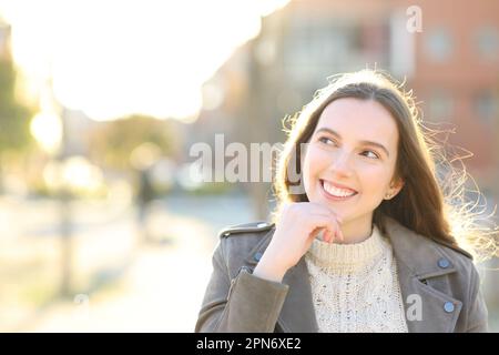 Portrait de face d'une femme heureuse qui pense à côté dans la rue Banque D'Images