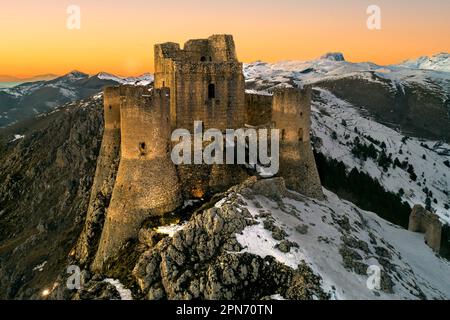 Vue aérienne de la Rocca di Calascio avec neige et illuminée par la lumière du coucher du soleil, derrière la chaîne du Gran Sasso et du Corno grande. Banque D'Images