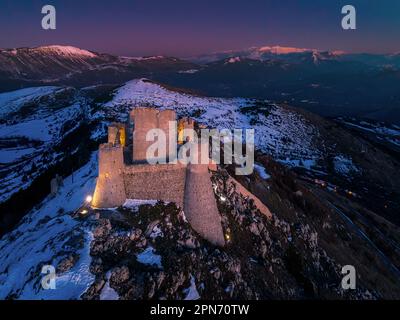 Vue aérienne de la Rocca di Calascio avec de la neige et éclairée par la lumière du coucher du soleil, en arrière-plan les montagnes du parc national de Maiella. Banque D'Images