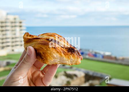 La nourriture maltaise locale appelée pastizz ou pastizzi. Personne main tenant une petite tarte en forme de diamant avec Malte Sliema ville sur fond bleu ciel et mer Banque D'Images