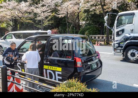 Avril 2023, Toyota JPN hybride taxi noir s'arrête à Tokyo pour prendre un tarif de dame et des portes ouvertes, Japon, Asie Banque D'Images