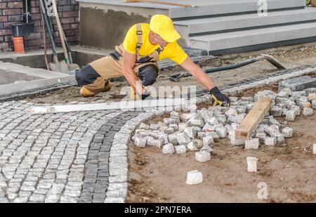 Entrepreneur professionnel construquant un passage en pierres de pavage devant la maison. Thème de l'amélioration de l'habitat. Banque D'Images