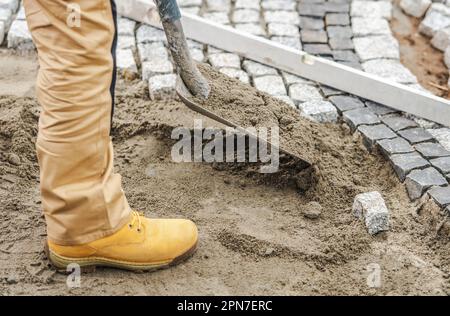 Gros plan de l'entrepreneur professionnel avec une pelle préparer le sol pour la pose de pavés en créant un lit de sable. Thème industriel. Banque D'Images