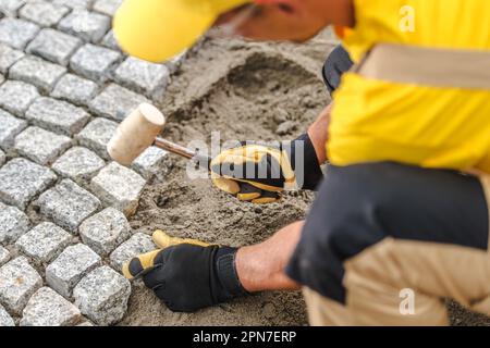 Gros plan de l'entrepreneur professionnel en uniforme jaune posant des pierres de pavage les jetant dans le sable. Thème de l'amélioration de l'habitat. Banque D'Images