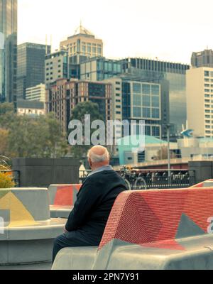 Melbourne, Australie - vieil homme assis sur un banc de béton et regardant les gratte-ciel de la ville Banque D'Images