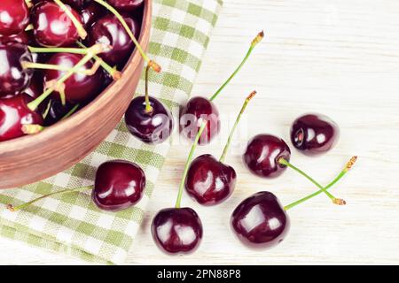 Cerises douces biologiques fraîches rouges mûres dans le bol en argile sur fond de bois blanc. Banque D'Images