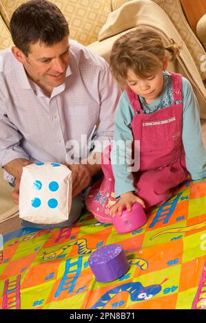 Père et jeune fille jouant avec un jeu de serpents et d'échelles d'intérieur surdimensionné Banque D'Images