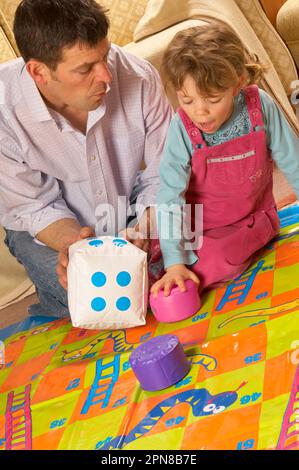 Père et jeune fille jouant avec un jeu de serpents et d'échelles d'intérieur surdimensionné Banque D'Images