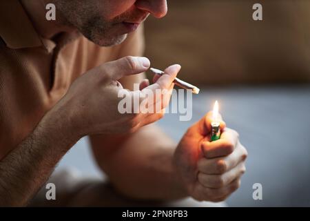 Vue latérale gros plan d'un adulte méconnaissable qui allume une cigarette tout en fumant à la maison à des fins thérapeutiques et thérapeutiques Banque D'Images