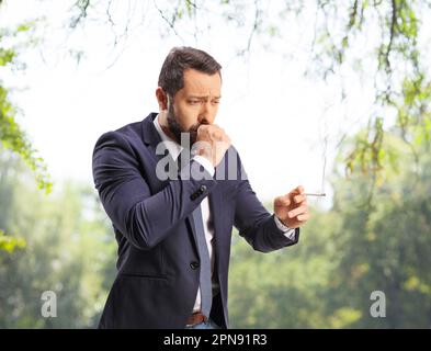 Homme fumant et toussant à l'extérieur dans un parc Banque D'Images