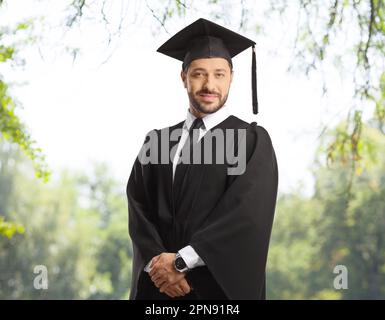 Homme portant une robe d'études supérieures et posant à l'extérieur dans un parc Banque D'Images