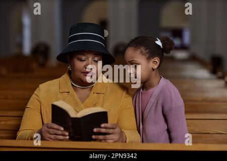 Grand-mère lisant la Bible à sa petite-fille pendant qu'ils sont assis sur le banc dans l'église Banque D'Images