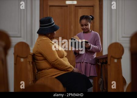 Petite fille afro-américaine lisant la prière de la Bible à sa grand-mère lors de leur visite à l'église Banque D'Images