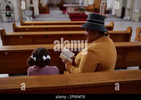 Grand-mère afro-américaine qui lit la Bible à sa petite-fille dans l'église, elle lui enseigne les coutumes chrétiennes Banque D'Images