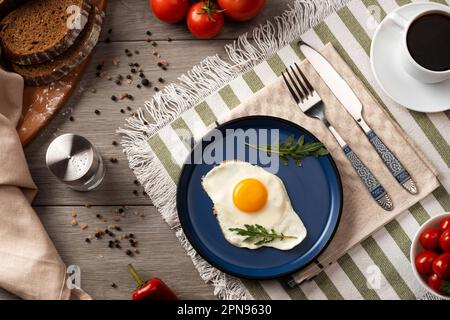 Œufs frits pour le petit déjeuner. Petit déjeuner sain avec des légumes et des herbes. Œuf frit sur une assiette bleue. Banque D'Images