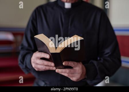 Gros plan du prêtre lisant le livre de la Bible pendant la cérémonie se tenant près de l'autel dans l'église Banque D'Images