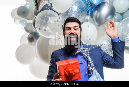 Un homme à barbe heureux avec ballons à hélium tient une boîte cadeau. Homme souriant célébrant son anniversaire. Fête. Beau homme d'affaires célébrant quelque chose Banque D'Images