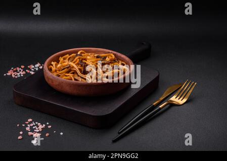 De délicieuses nouilles ou un udon aux champignons, au sel, aux épices et aux herbes sur une plaque en céramique sur fond de béton foncé Banque D'Images