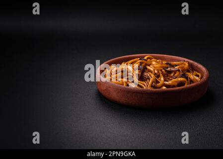 De délicieuses nouilles ou un udon aux champignons, au sel, aux épices et aux herbes sur une plaque en céramique sur fond de béton foncé Banque D'Images