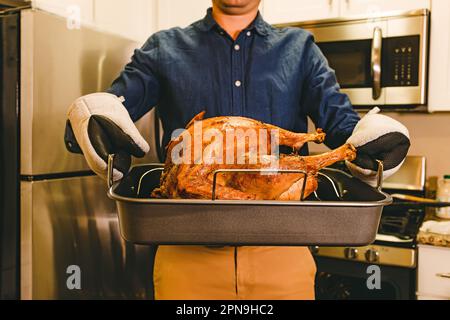 Homme méconnaissable tenant un plateau avec une dinde croustillante rôtie, préparation de nourriture de Thanksgiving à la maison Banque D'Images