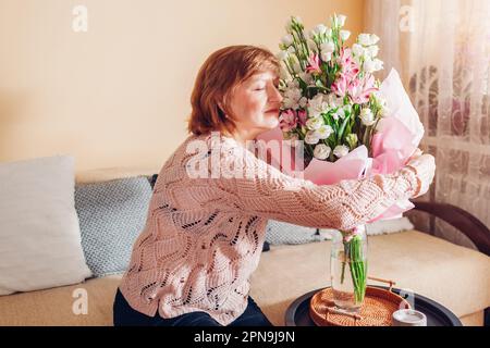 Bonne surprise de la fête des mères. Femme âgée sentant un bouquet de fleurs d'eustoma à la maison. Cadeau pour les vacances de printemps Banque D'Images