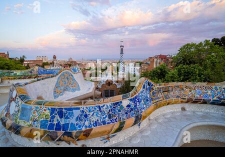 Bancs avec mosaïque colorée, bâtiment d'entrée à l'arrière, Pabellon de administracion, vue sur la ville dans la lumière du soir, Parc Gueell Banque D'Images