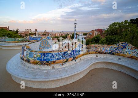 Bancs avec mosaïque colorée, bâtiment d'entrée à l'arrière, Pabellon de administracion, vue sur la ville dans la lumière du soir, Parc Gueell Banque D'Images