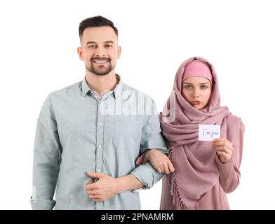 Une femme musulmane meurtrisée tenant du papier avec du texte, je Vais BIEN et son mari sur fond blanc. Concept de violence domestique Banque D'Images