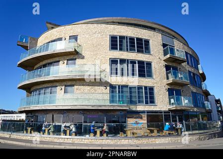 Touristes se détendant au café Windy Corner dans le bâtiment Ellipse sur le quai, West Bay, Dorset, Royaume-Uni, Europe. Banque D'Images