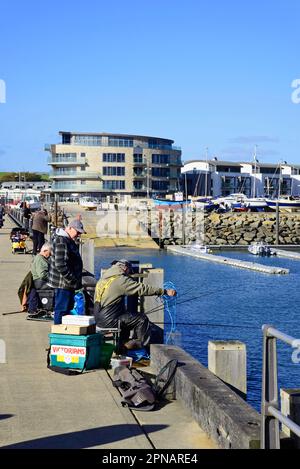 Des hommes pêchant depuis la jetée du port avec des bâtiments de ville à l'arrière, West Bay, Dorset, Royaume-Uni, Europe. Banque D'Images