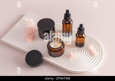 un ensemble de bouteilles cosmétiques en verre foncé avec crème et sérum sur un podium de plâtre de soulagement sous forme d'arche. soins naturels Banque D'Images