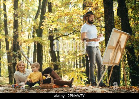 Tirer de la vie. Peintre avec famille se détendre en forêt. Peinture dans la nature. Démarrer une nouvelle photo. Capturez l'instant. Beauté de la nature. Homme barbu Banque D'Images